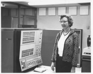 Black and white photo of Winifred Asprey, Vassar class of 1938, founder of the Computer Science Department, standing in front of an old computer system.