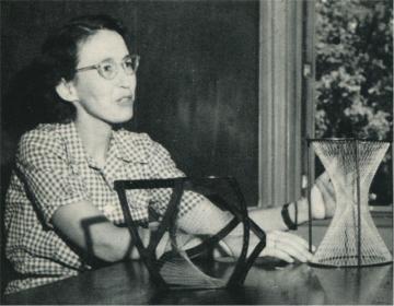 Old black and white photo of Professor Winifred Asprey VC Class of 1938 Ph.f6.11 wearing a checkered shirt, sitting at a table with two mathematical models.