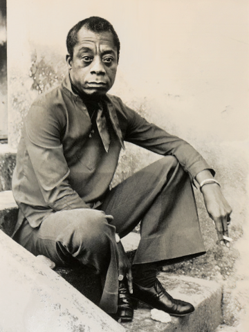 A black-and-white portrait photo of a man, sitting on some stone steps facing the camera.