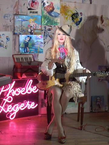 Artist Phoebe Legere ’81 seated on a chair holding a guitar