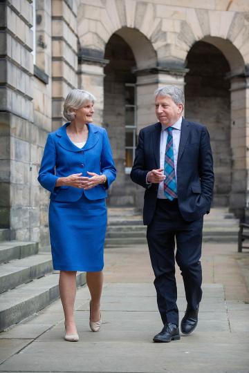 President Elizabeth H. Bradley and Peter Mathieson, Principal and Vice Chancellor of the University of Edinburgh (Scotland) walking and talking with stone buildings in the background.