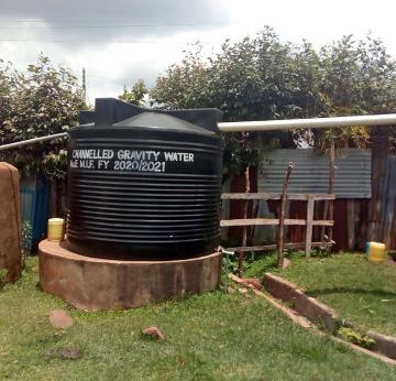 Large black water tank on grassy area with trees and metal fence in the background