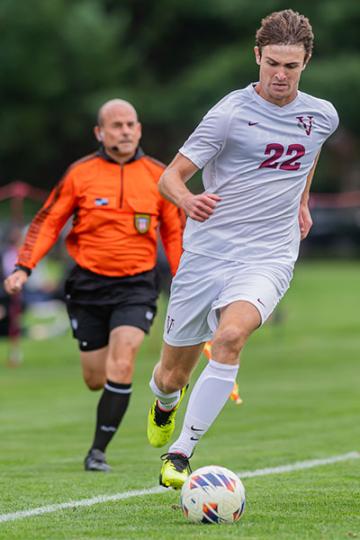 Duncan Keker ’25 kicking the ball with a ref behind him.