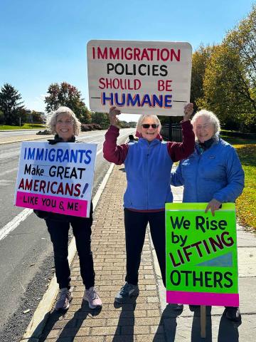 Three people on the side of the road holding signs that read: Immigrant policies should be humane; we rise by lifting others; and Immigrants make great americans