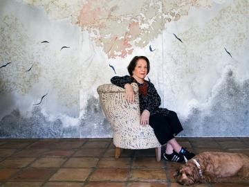 Mira Lehr seated in front of a large abstract painting with a dog at her feet.