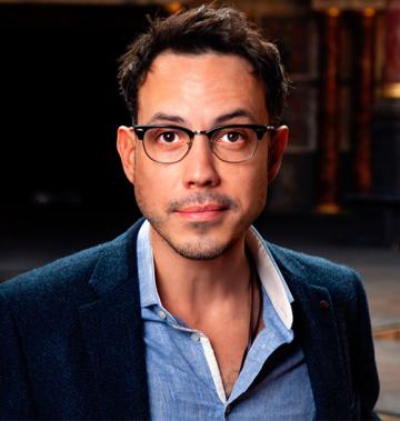 Man with black hair, glasses, blue shirt, and dark overcoat.