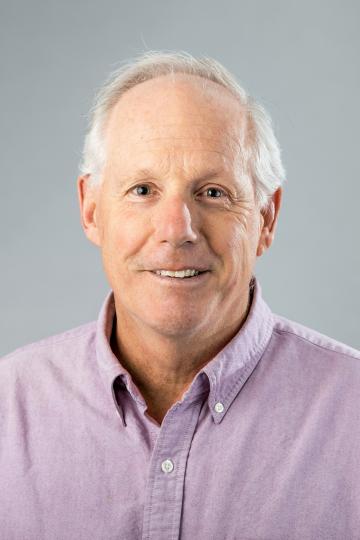 Portrait of a person with balding grey hair and a light purple shirt.