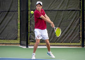 Person in Vassar tennis uniform preparing to hit a forehand tennis ball on a green tennis court with a fence in the background.