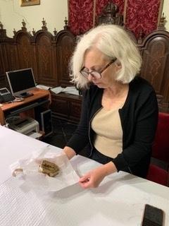 Julie Harris sitting at a desk, looking at a gold object wrapped in tissue paper.