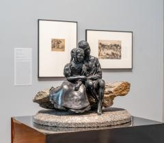 A photo of an iron sculpture of two people sitting on a large rock.