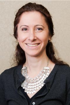 Bojana Zupan wearing a black shirt and large gold necklace against a light colored background.