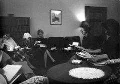 Black and white photo of Inez Scott Ryberg in her apartment with other people sitting at a table and on a couch.