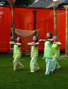 Photo of a performance of Oedipus at Colonus' in 2007 of people wearing green clothing and masks in front of a red draped background.