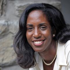 A person with long, black hair and a white formal shirt smiles at the viewer.