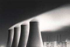 A monochrome print of four tall conical towers of a nuclear power station with steam coming out of them.