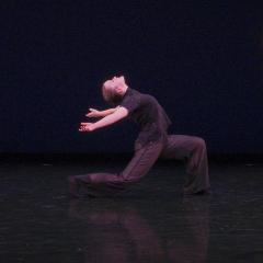 Photo of dancer wearing black clothes on a black stage with black background.