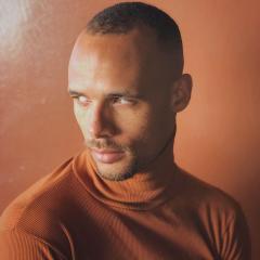 Head and shoulders photo of Mike Tyus wearing an orange shirt with a light orange background.