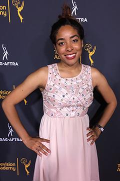 Amanda Jones in a pink, sleeveless evening dress, smiling at the camera with her hands on her hips.