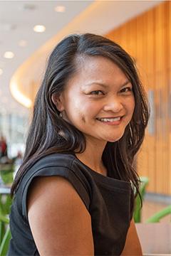 Michele Tugade wearing a sleeveless black dress smiling broadly at the camera, her long, dark hair parted on the side.