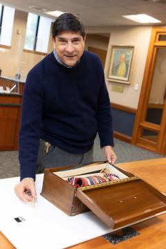 Man standing at a table in front of a box and a pin/broach