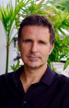 Dr. Denis Regnier, wearing a black shirt standing in front of a green plant