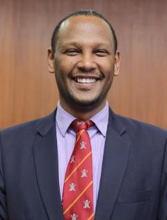 Dr. Abebe Bekele, wearing a dark blue jacket, light purple patterned shirt and red tie