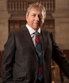 Dr. Peter Mathieson, Principal and Vice Chancellor of the University of Edinburgh wearing a brown suit, white shirt and red and blue patterned tie