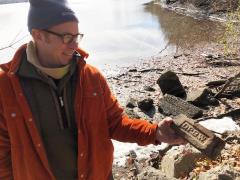 Man in an orange jacket standing near rocks on a beach