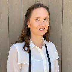 Hillary Lyons wearing a white collar shirt standing in front of a wood board building