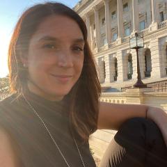 Kara Voght in front of a three story white brick building wearing a black short sleeve shirt and silver necklace