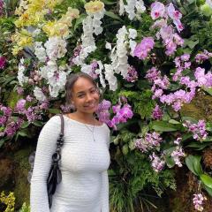 Lola Wright wearing a white shirt standing in front of a large flowering bush