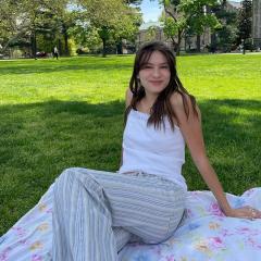 Olivia Chang wearing white sleeveless shirt and striped pants lying on a blanket on the grass