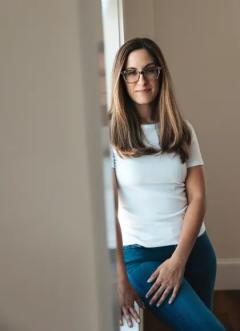 Michelle Horton wearing a white t-shirt and jeans, leaning against a beige colored wall.