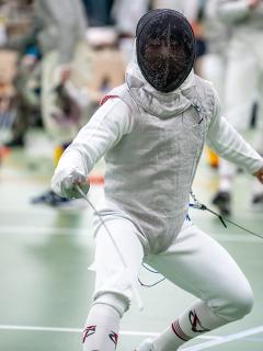 Action shot of Isaiah Kim wearing a fencing mask and thrusting his sword.