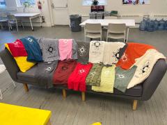 A bunch of screen printed t-shirts laid out on a couch.