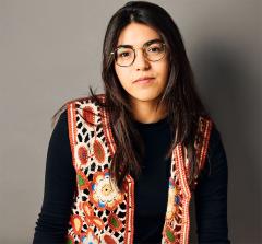 Miranda Cornell wearing a long sleeve black shirt and a colorful knit vest with flowers, eyeglasses and has long dark hair.