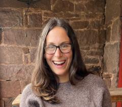 Sydney Forman wearing a light brown knit sweater, eyeglasses and has long light brown hair.