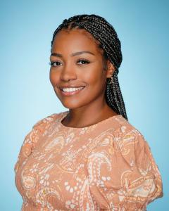 Lily Harford wearing a peach and white patterned top and hair in braids against a blue background.