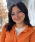 Woman with black hair and orange shirt smiling outside