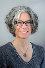 Susan G. Blickstein wearing a gray sweater and silver necklace against a gray background.