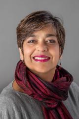 Mita Choudhury wearing a gray shirt and black and red scarf against a gray background.