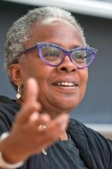 A person wearing a black shirt and purple eyeglasses with arm extended against a dark background.