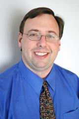 Eric S. Eberhardt wearing a blue shirt and multi colored tie against a light background.