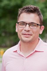 Joshua R. de Leeuw wearing a pink collared shirt with trees in the background.