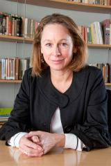 Tracey Holland wearing a black shirt over a white one with a bookshelf in the background.
