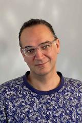 A portrait of a person with dark hair and glasses looking at the camera.