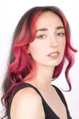 A photograph of a person with long, crimson hair wearing a black tank top and looking at the camera
