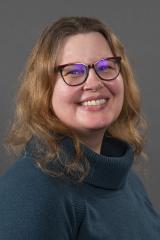 Woman in a blue turtleneck sweater and glasses smiling.