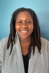 Person with long black dreadlocks with a patterned white suit jacket and black v-neck t-shirt