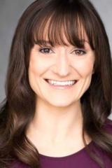 A photo portrait of a person with long, straight, brown hair and a purple shirt. The person is smiling at the viewer.